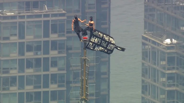 Angela Nikolau and Ivan Kuznetsov standing on the Empire State Building antenna in New York City on July 1, 2026, displaying a black peace banner
