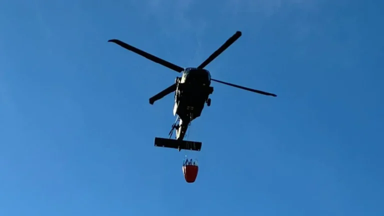 Helicopter dropping water over a smoky, rocky, wooded ridge during a wildfire response in western Massachusetts