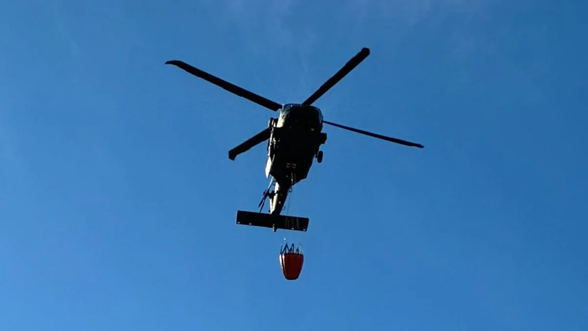 Helicopter dropping water over a smoky, rocky, wooded ridge during a wildfire response in western Massachusetts