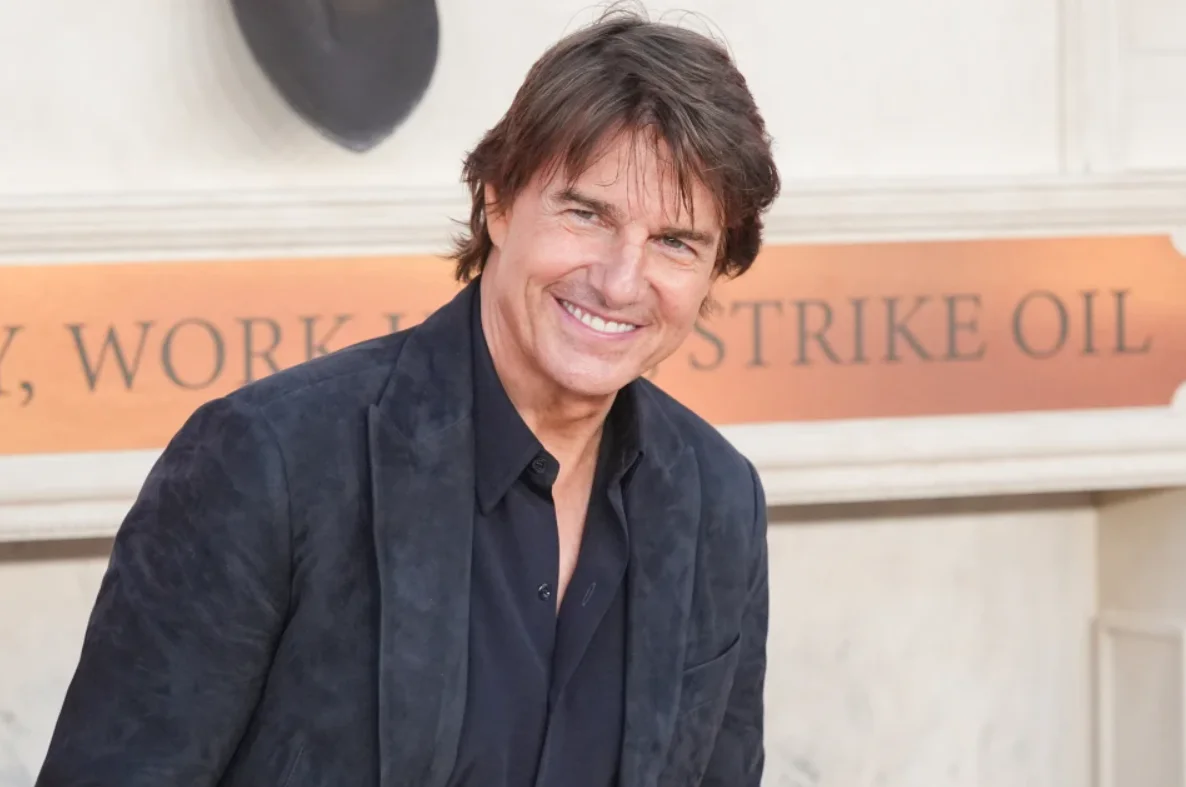 Actor Tom Cruise smiling in a black dress shirt and dark suit jacket at an entertainment event.