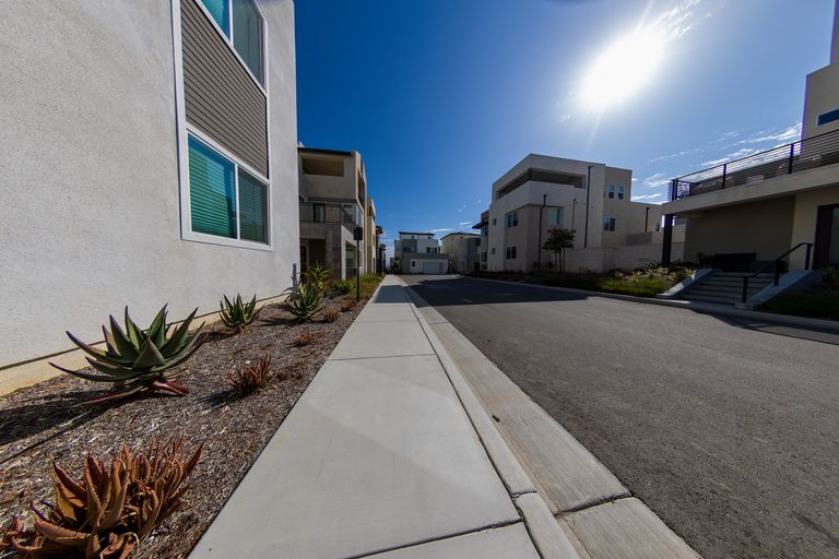 Wide-angle view of a sunny suburban street with modern homes and a clear blue sky, capturing peaceful residential living.